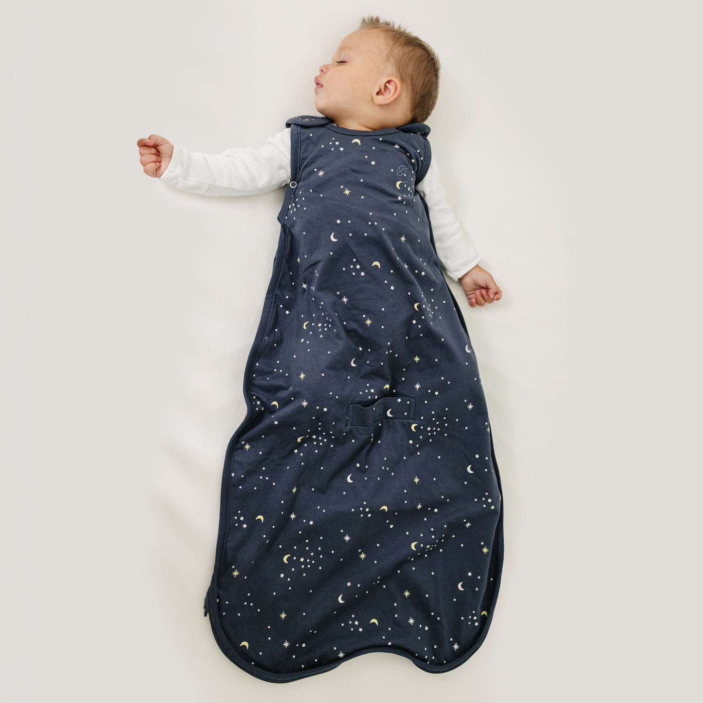 Baby sleeping in a dark blue sleep bag with celestial pattern on a light background