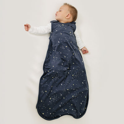 Baby sleeping in a dark blue sleep bag with celestial pattern on a light background