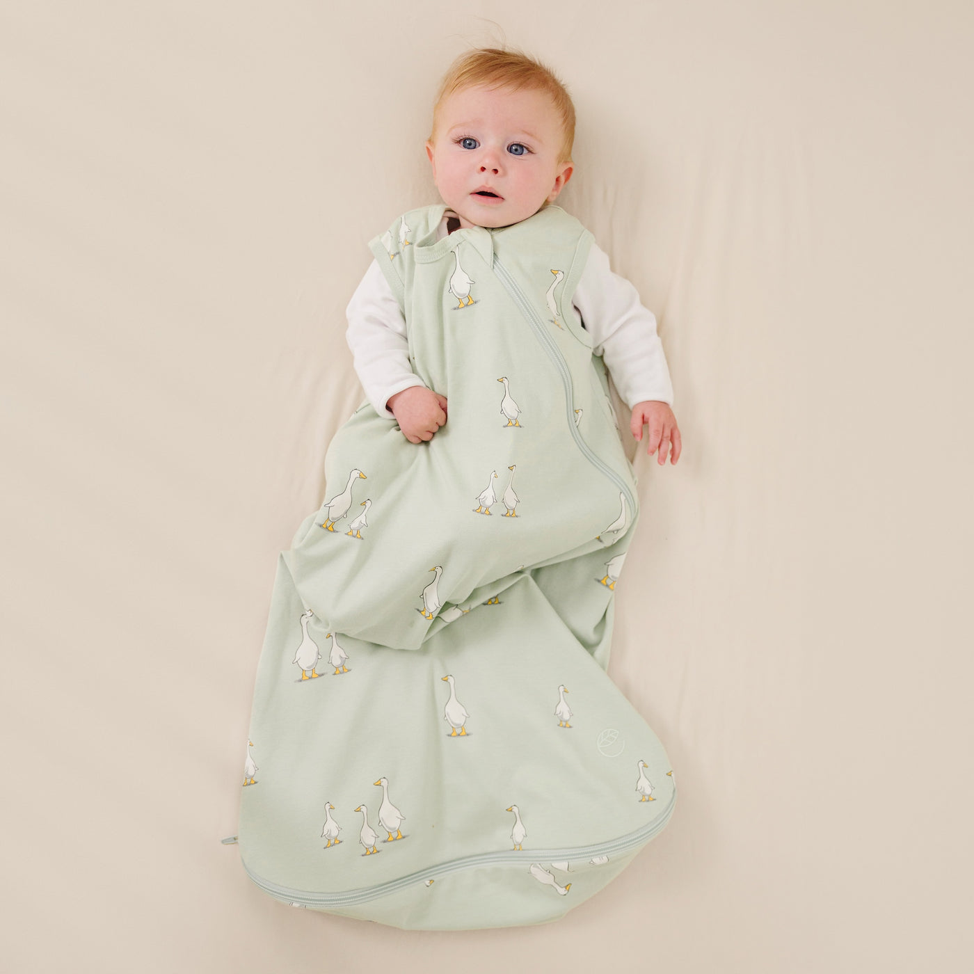 Baby wrapped in a green sleeping bag with duck pattern on a beige background