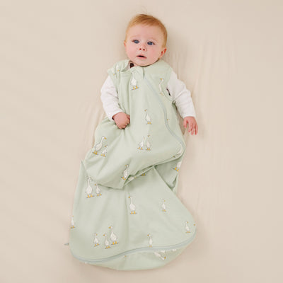 Baby wrapped in a green sleeping bag with duck pattern on a beige background