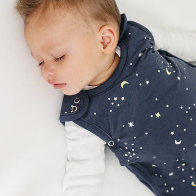 Baby wearing a navy blue sleep sack with celestial patterns on a white background