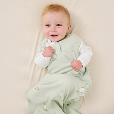 Baby wearing a light green Ecolino sleep sack with duck patterns on a beige background