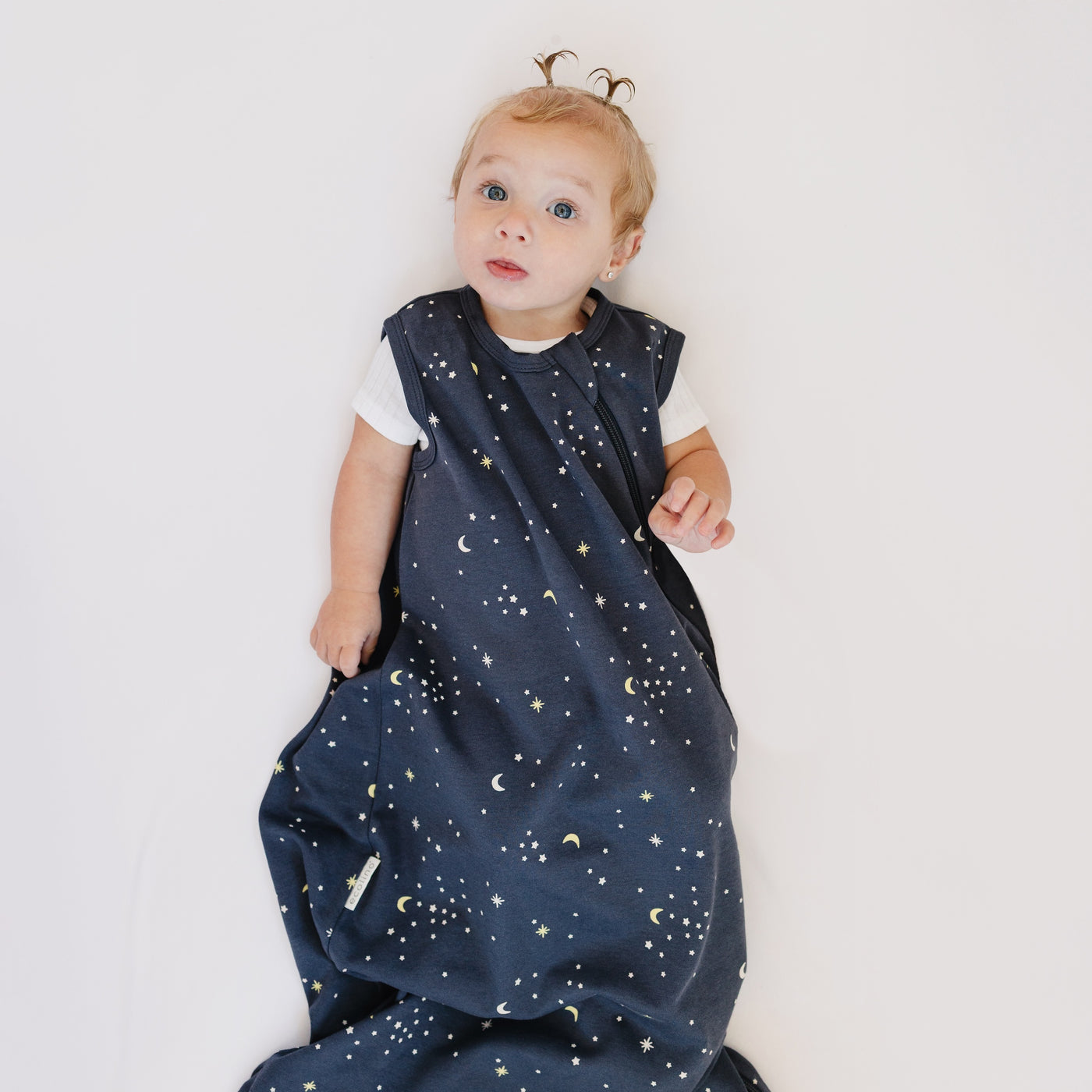 Baby wearing a dark blue Ecolino sleep bag with star and moon pattern on a white background