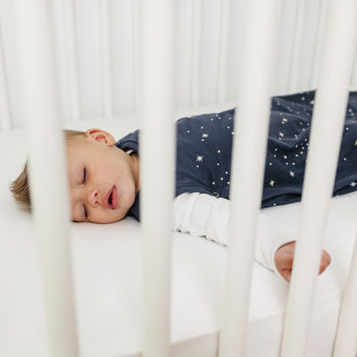 Child sleeping in a crib with white bedding and a star-patterned Ecolino Sleep Sack.