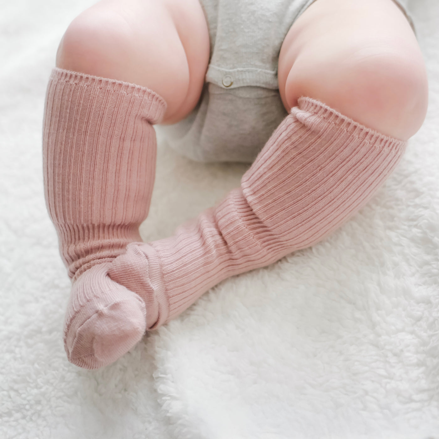 Baby legs wearing pink Woolino wool socks on a white surface