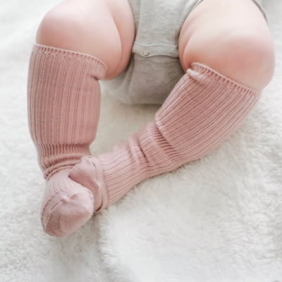 Baby legs wearing pink Woolino wool socks on a white surface