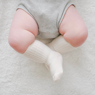 Close-up of a baby's legs wearing white wool socks on a soft surface